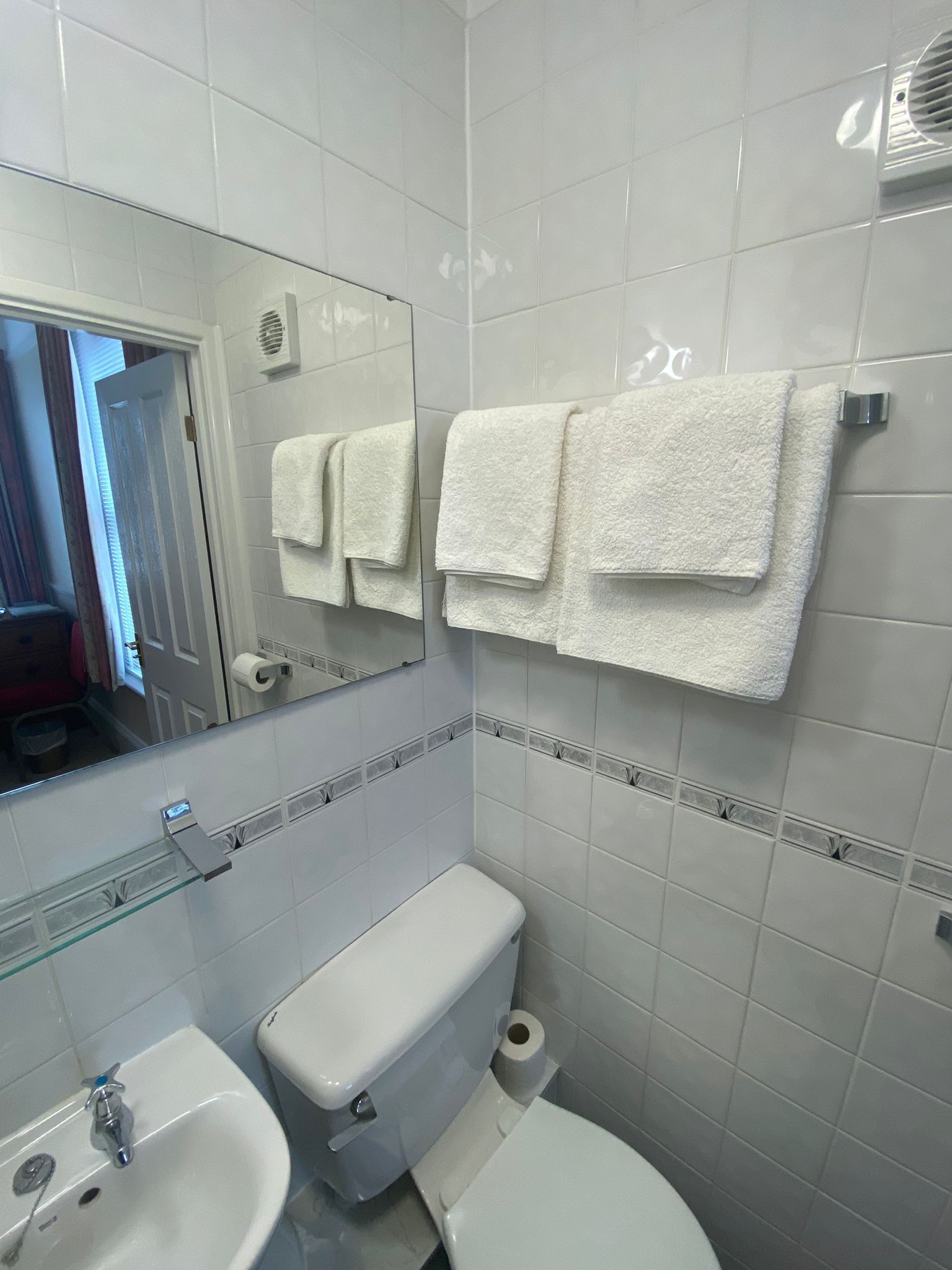 A bathroom with white tiles, a toilet, a sink, and a mirror.