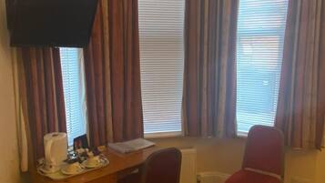 A hotel room with a desk, two chairs, a TV, and a bed.