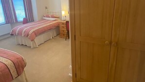Een slaapkamer met twee bedden, een houten kledingkast, een nachtkastje met een lamp en een raam met gordijnen.