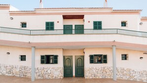 A two-story building with a stone facade, green doors, and a balcony with a railing. - Bluesea Cabo de Baños (Ciutadella de Menorca)