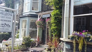 A guest house named Melrose with a signboard, a bay window with hanging flowers, and outdoor seating. - Melrose Guest House (Ambleside)