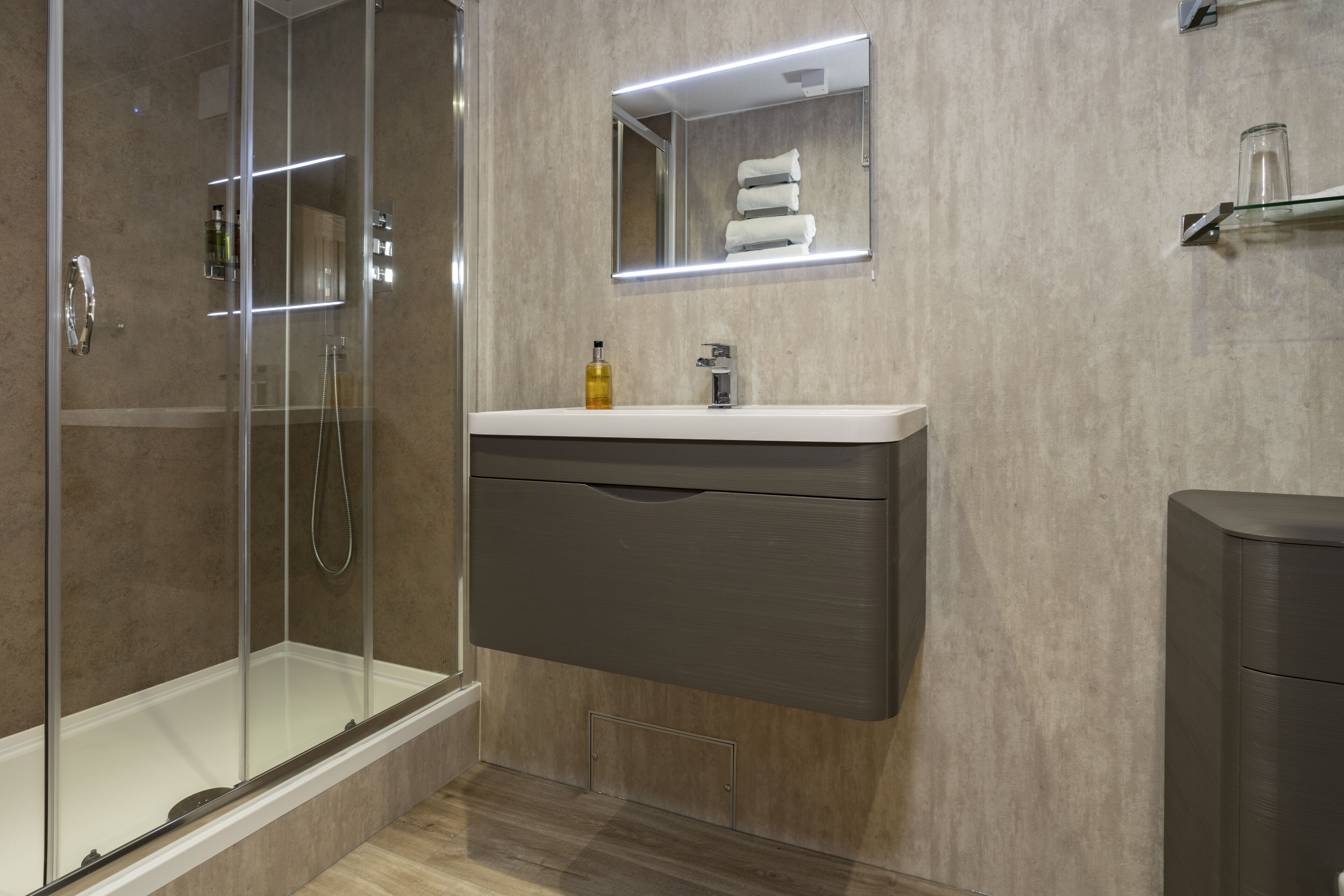 A modern bathroom with a glass-enclosed shower, a vanity with a mirror, and a glass shelf.