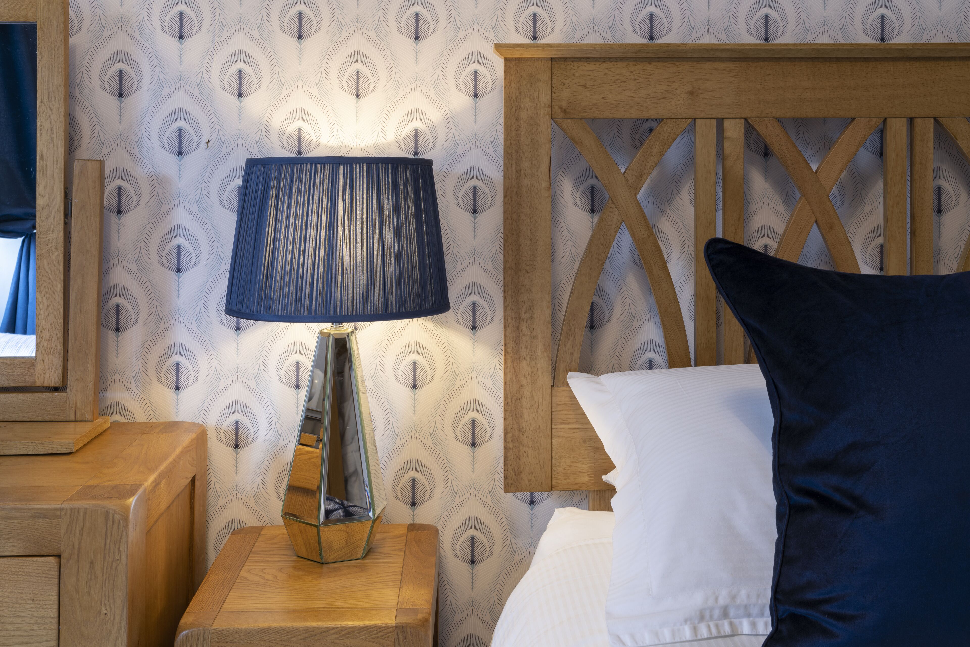 A neatly made bed with a wooden headboard, a bedside lamp, and a patterned wallpaper.