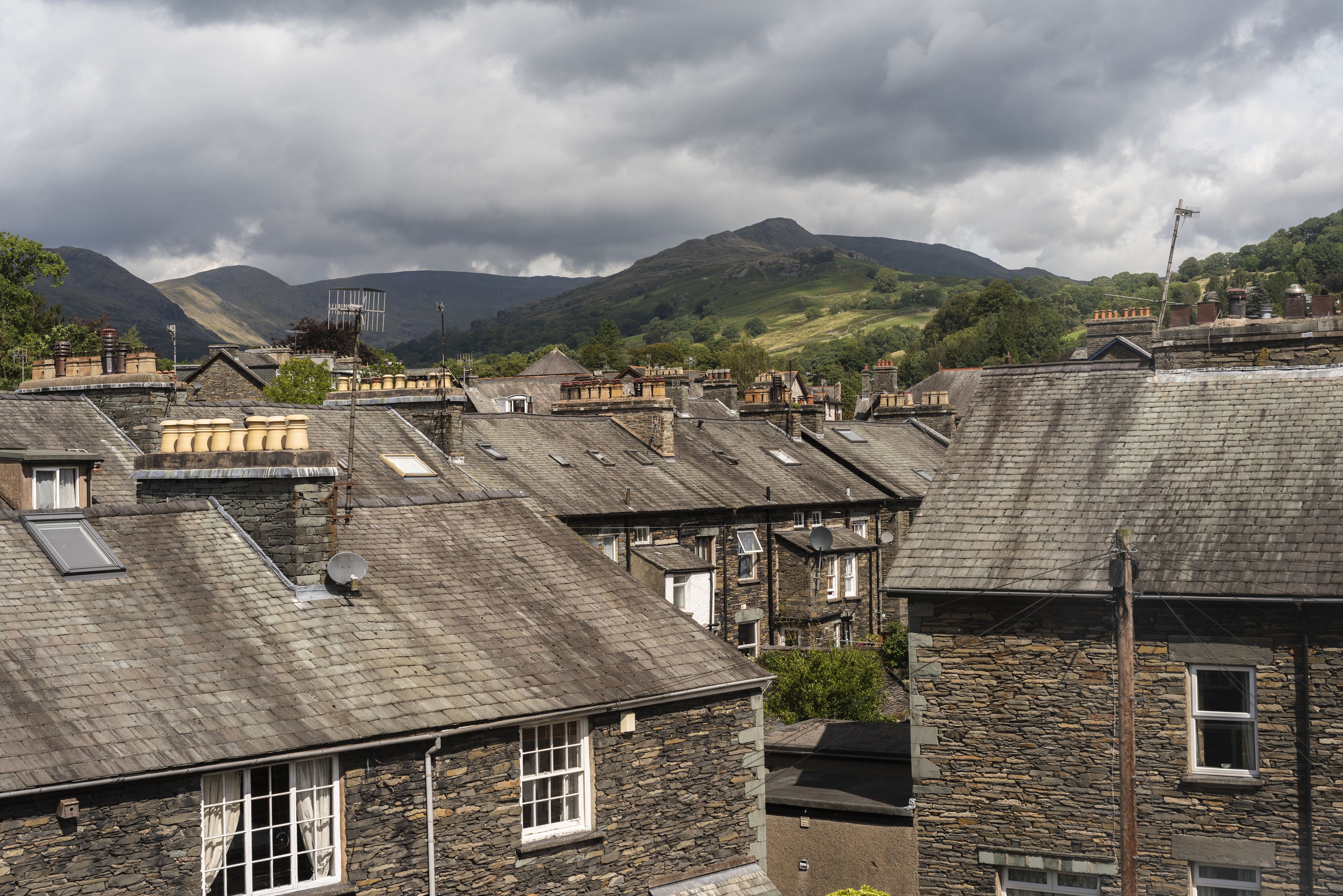 A row of stone buildings with flat roofs, some with satellite dishes, and a mountainous backdrop.