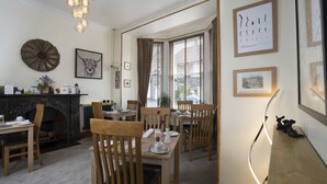 A dining area with wooden tables and chairs, a fireplace, and framed artwork on the walls. - Melrose Guest House (Ambleside)