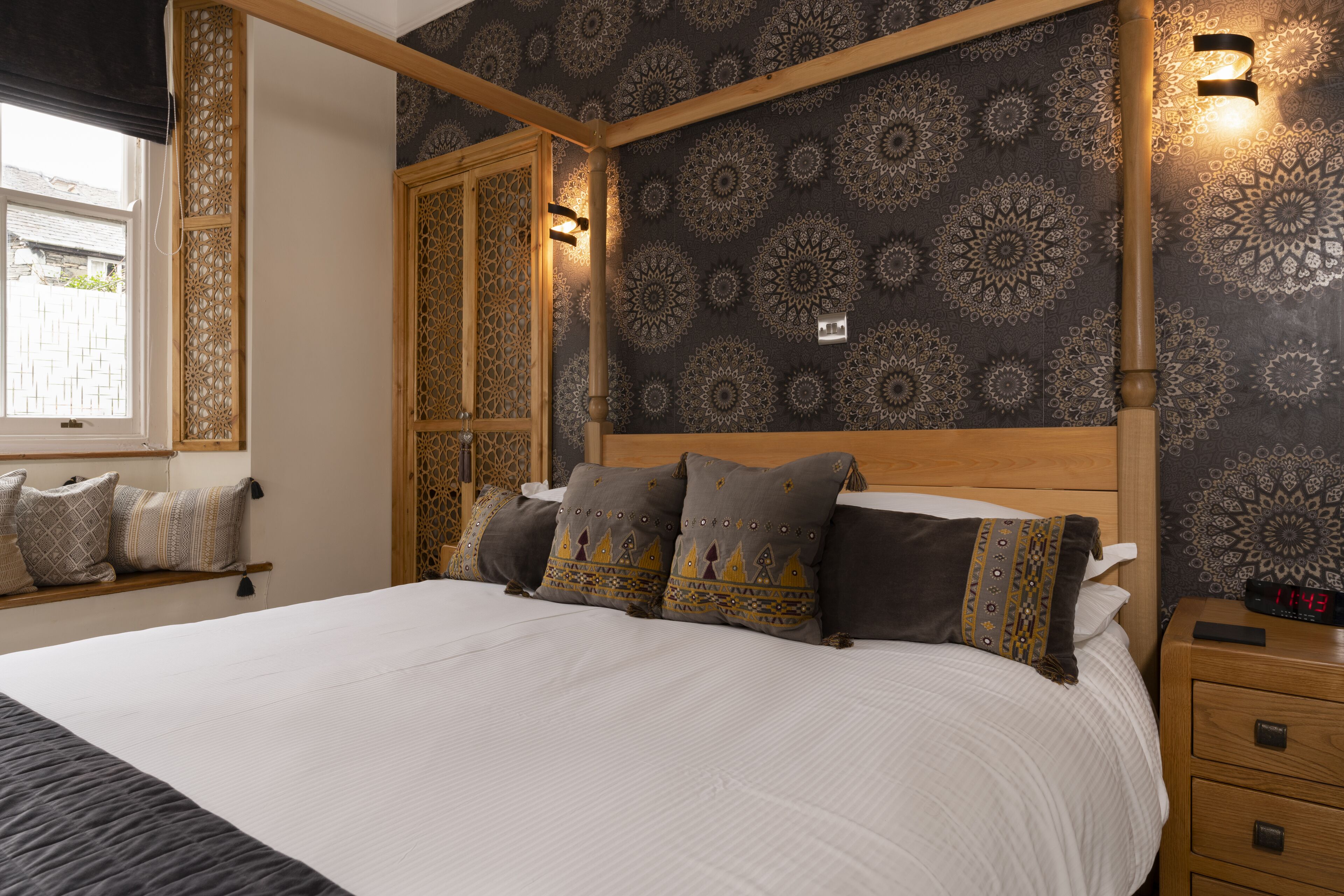 A bedroom with a large bed, patterned wallpaper, and a wooden headboard.