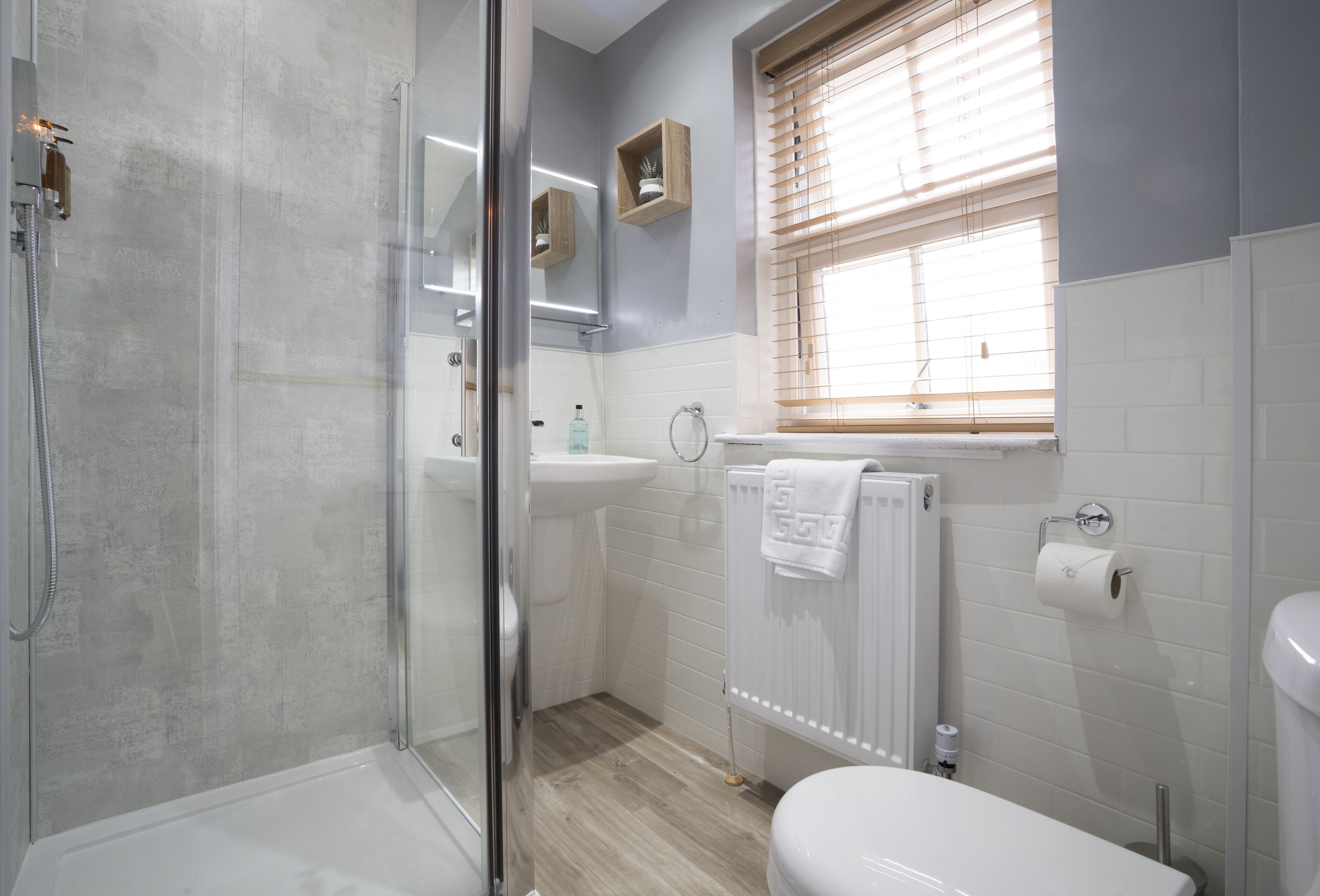 A bathroom with a glass shower enclosure, a sink, a toilet, and a window with blinds.