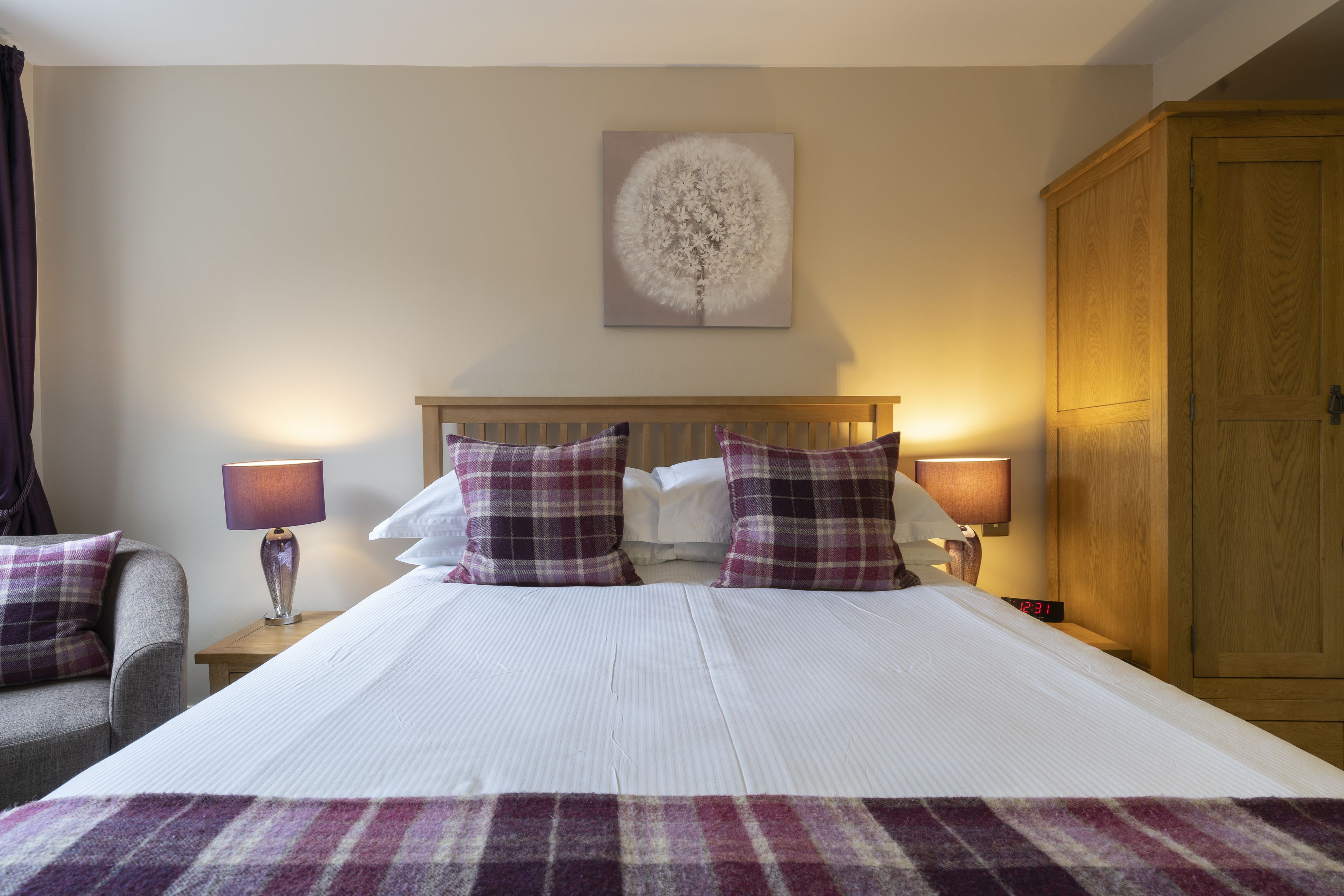 A hotel room with a large bed, two bedside lamps, a wooden wardrobe, and a wall-mounted artwork.
