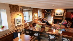 A cozy restaurant with stone walls, wooden tables, and chairs. There are candles on the tables, and a fireplace in the background. - The Mousetrap Inn (Cheltenham)