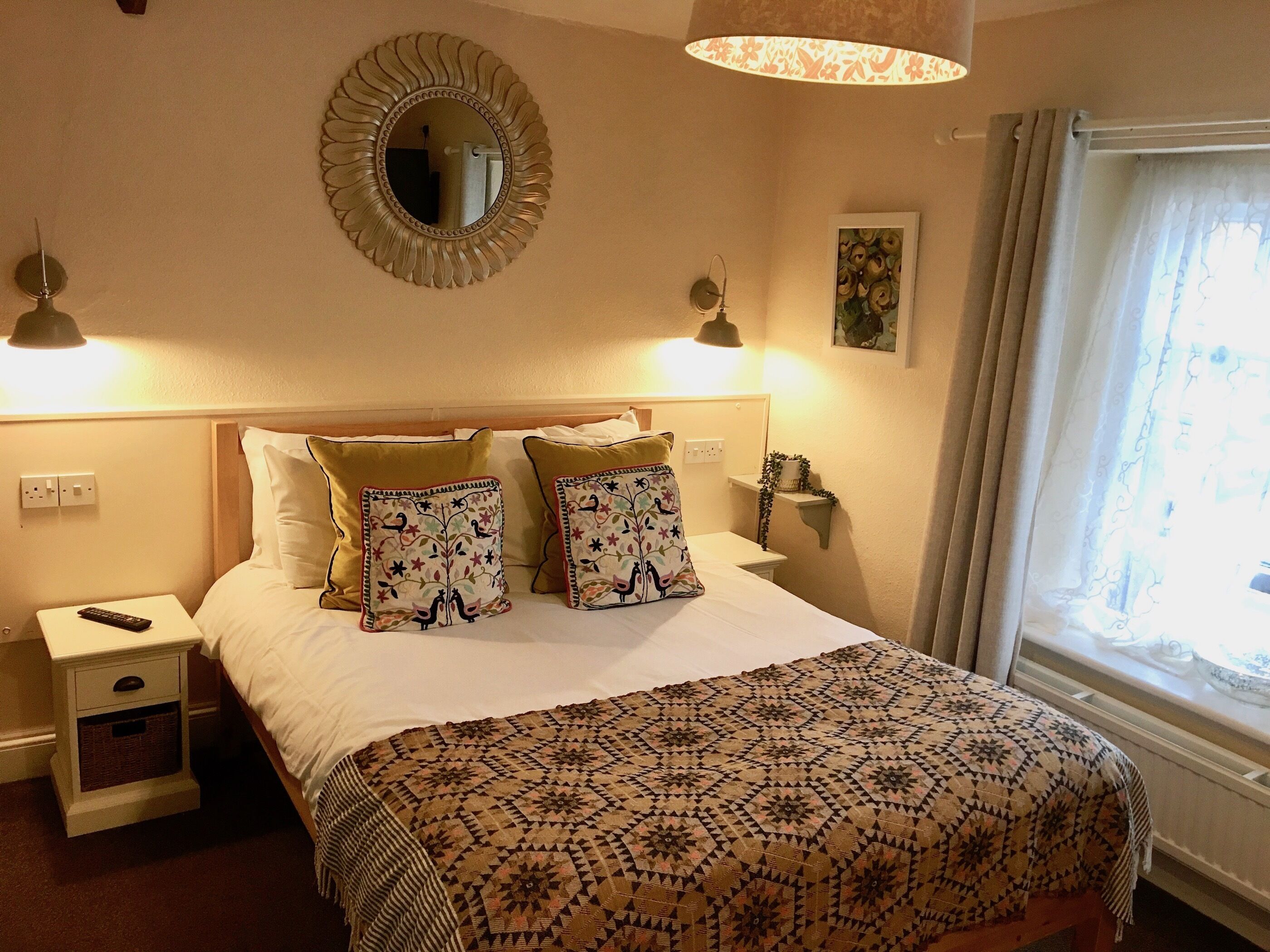 A neatly arranged hotel room with a bed, bedside tables, a mirror, and a window with curtains.