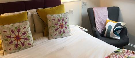 A bedroom with a bed, a chair, a skylight, and a shelf with books.