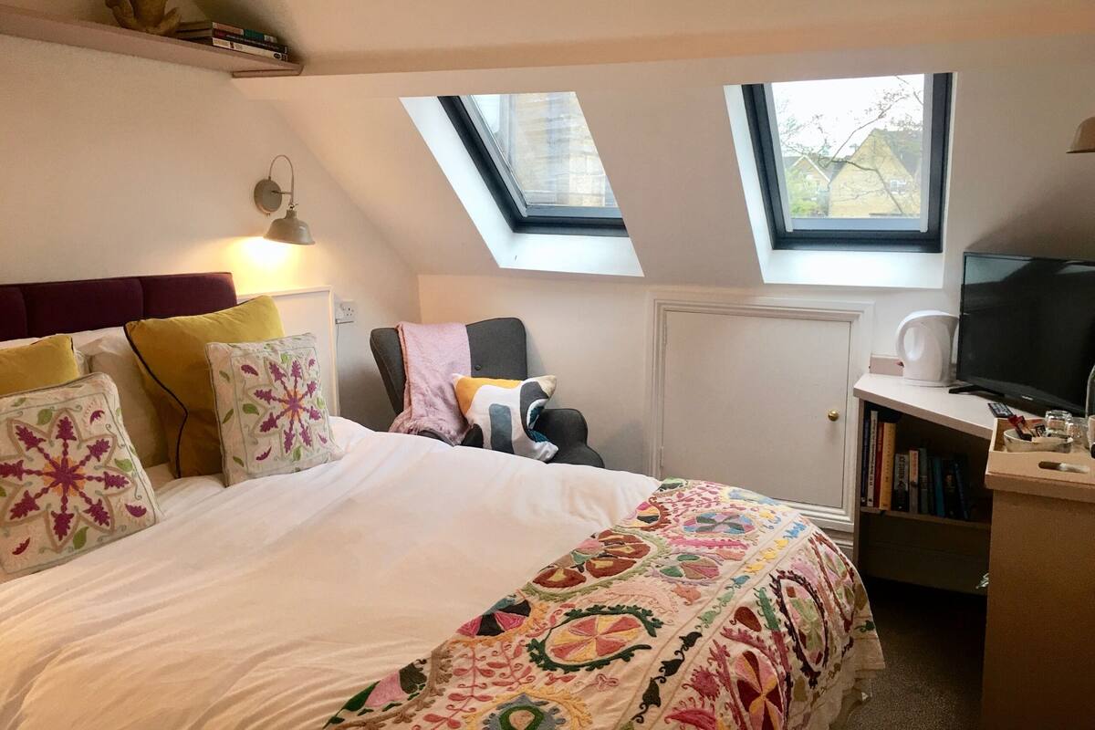 Quarto com uma cama, uma cadeira, uma televisão e uma estante de livros.