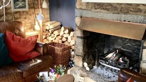 A cozy living room with a stone fireplace, a leather sofa, a wooden coffee table, and a basket of firewood. - The Mousetrap Inn (Cheltenham)