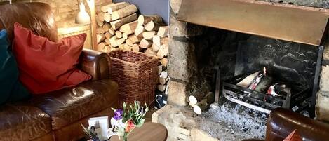 Un salon chaleureux avec une cheminée en pierre, un canapé en cuir, une table basse en bois et un panier de bois de chauffage.
