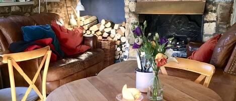 Un salon chaleureux avec une cheminée, une table ronde en bois et des sièges confortables.
