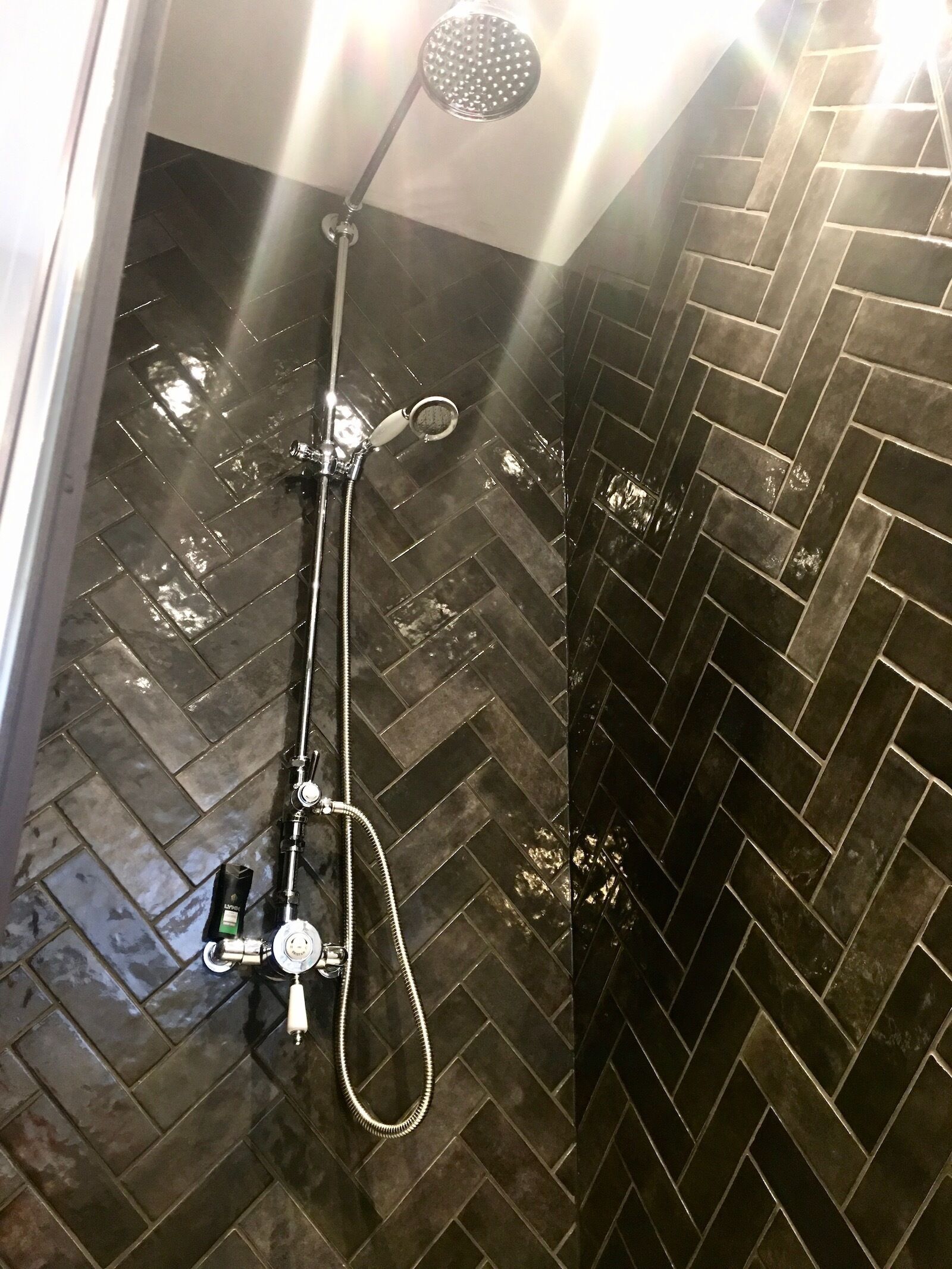 A shower with a handheld showerhead and a handheld sprayer, a handheld soap dispenser, and a handheld shampoo bottle.