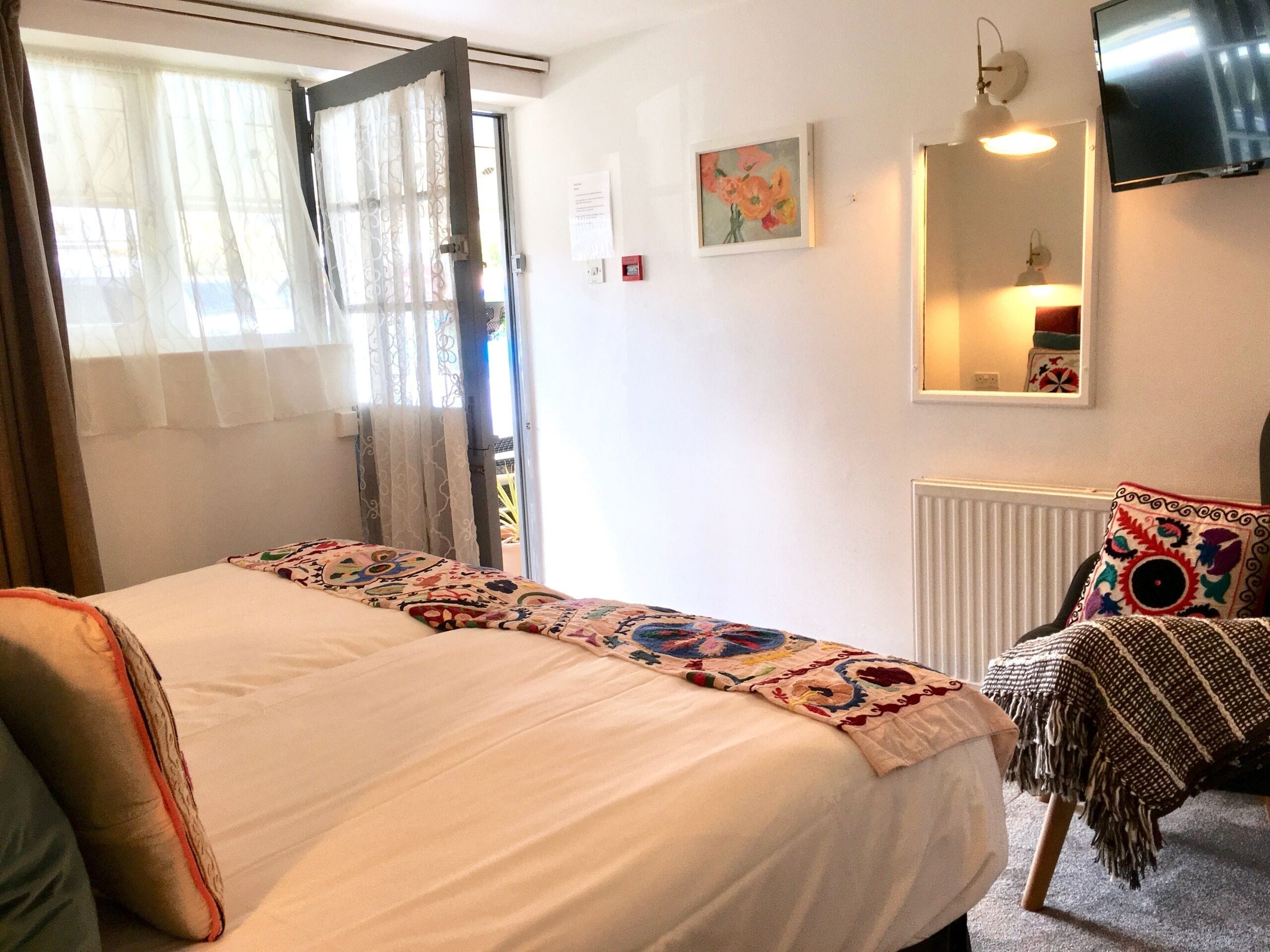 A bedroom with a bed, a window with curtains, a painting, a mirror, and a television.