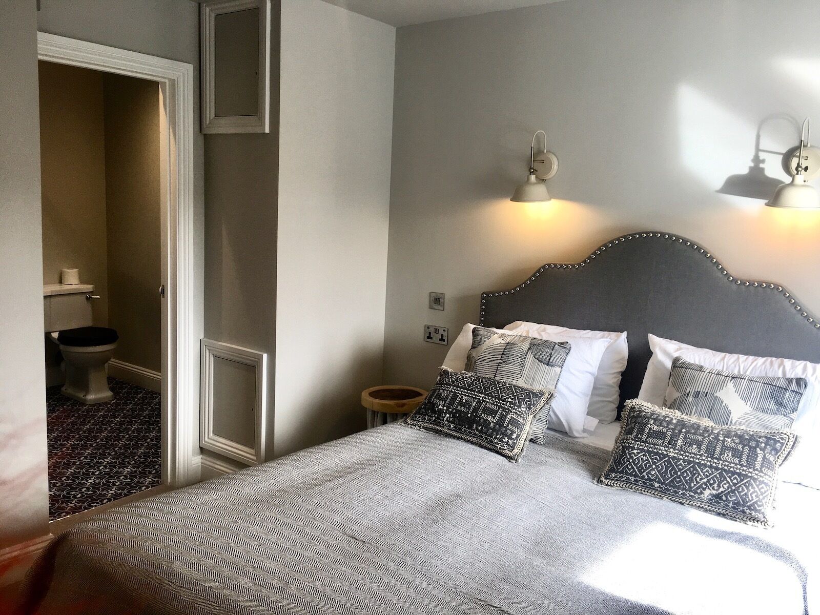 Une chambre à coucher avec un lit, des lampes de chevet, une table de chevet et une salle de bain visible à travers une porte ouverte.