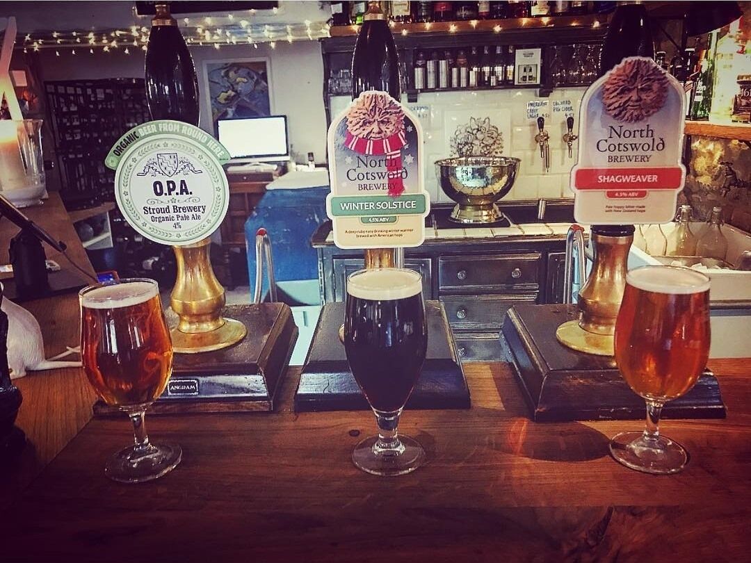 Three taps with different beer labels and three glasses of beer on a bar counter.