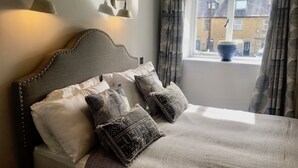 A neatly made bed with a headboard, several pillows, and a window with curtains. - The Mousetrap Inn (Cheltenham)
