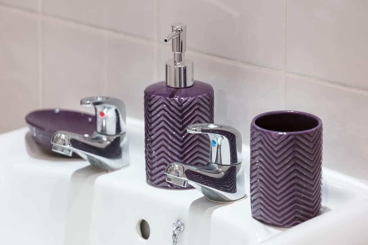 A bathroom sink with a chrome faucet, a purple soap dispenser, and a matching purple mug.