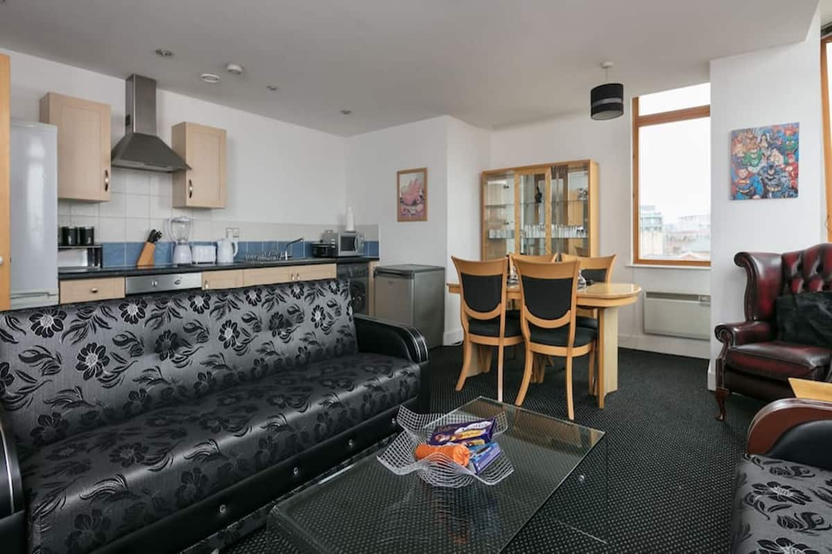 A compact living space with a kitchenette, a sofa, a dining table with chairs, and a leather armchair.