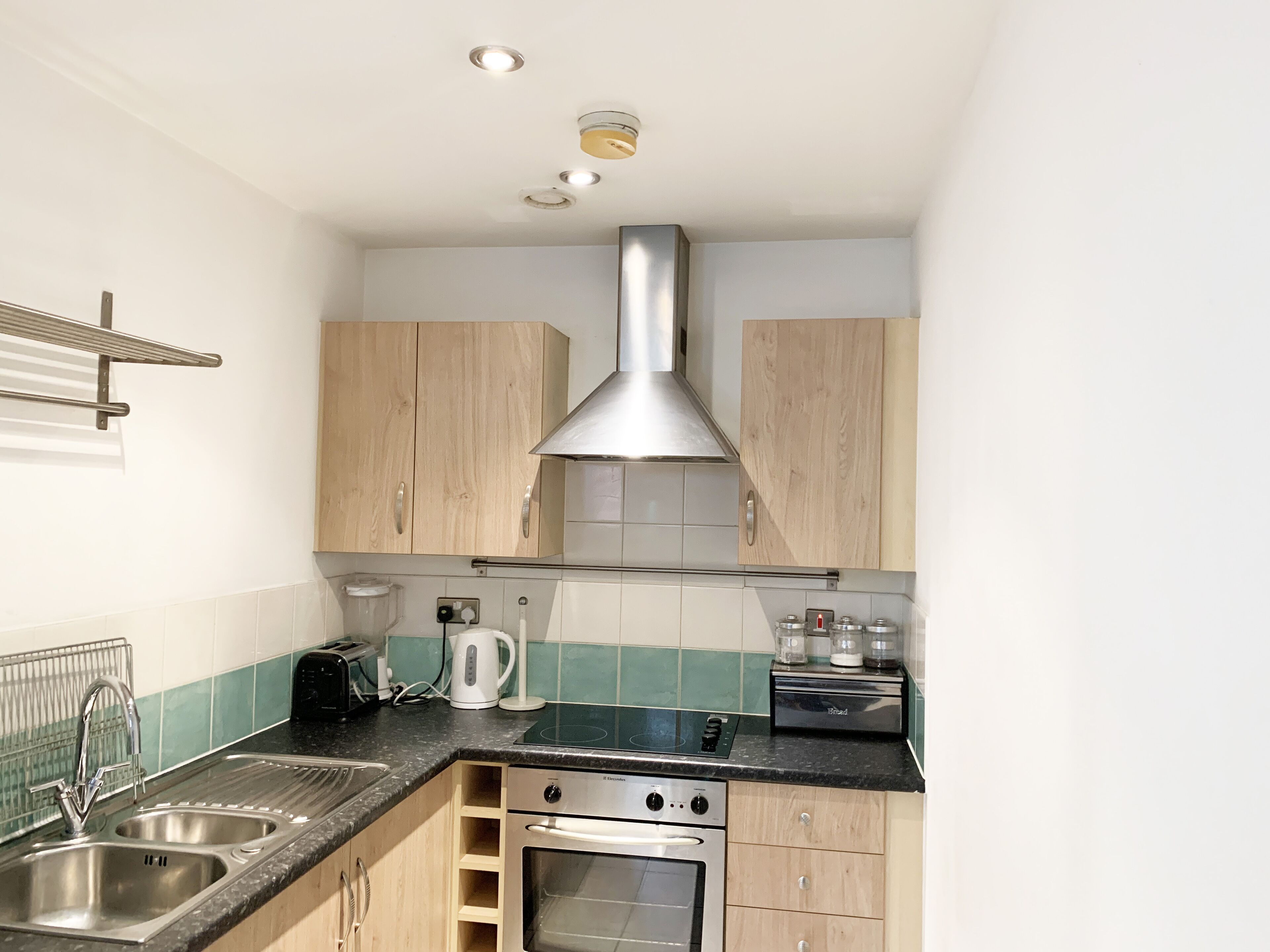 A compact kitchen with wooden cabinets, a stainless steel sink, a built-in oven, and a black countertop.