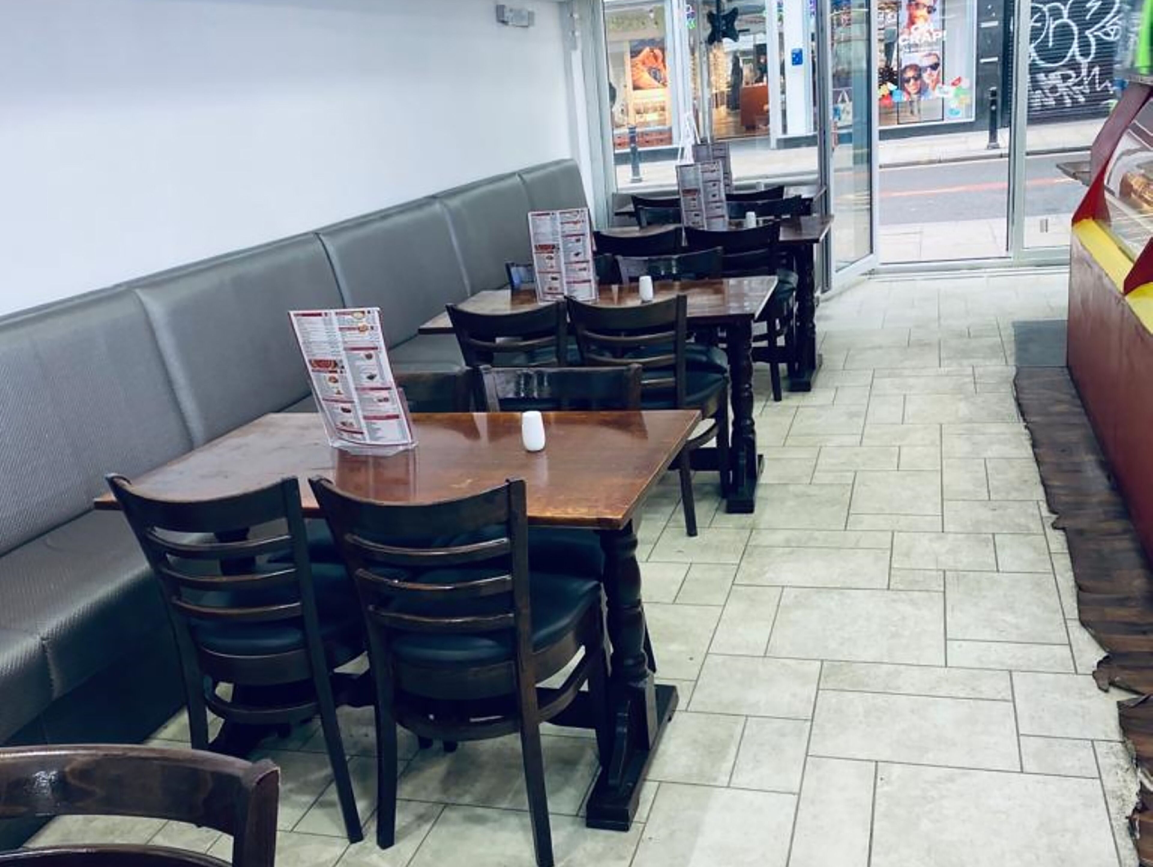 A restaurant interior with booths and tables, a tiled floor, and a menu stand.