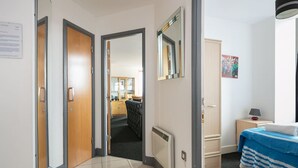 A hotel room with a bed, a nightstand, a mirror, and a door leading to a hallway. - My-Places Serviced Apartments (Manchester)