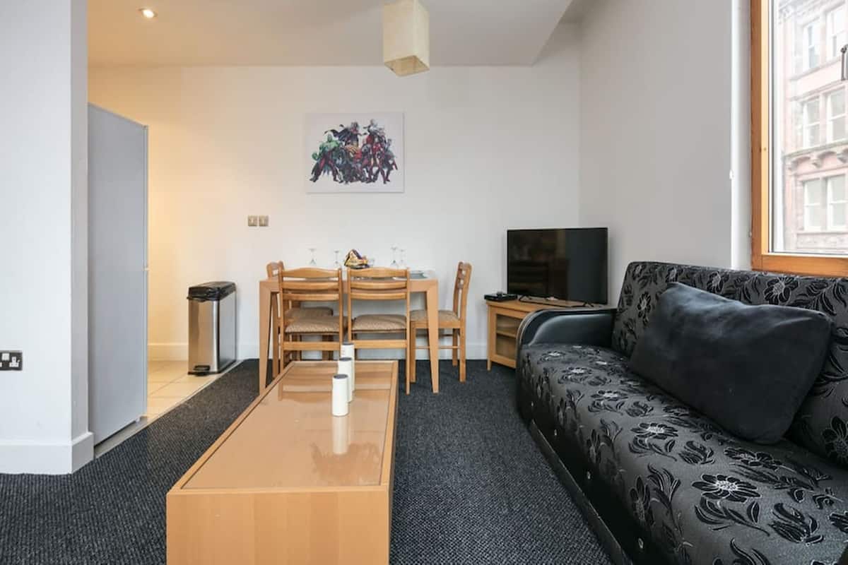 A modern living room with a sofa, a dining table with chairs, a TV, and a painting on the wall.