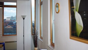 A room with large windows, a view of a cityscape, a tall floor lamp, and a vase with a plant. - My-Places Serviced Apartments (Manchester)