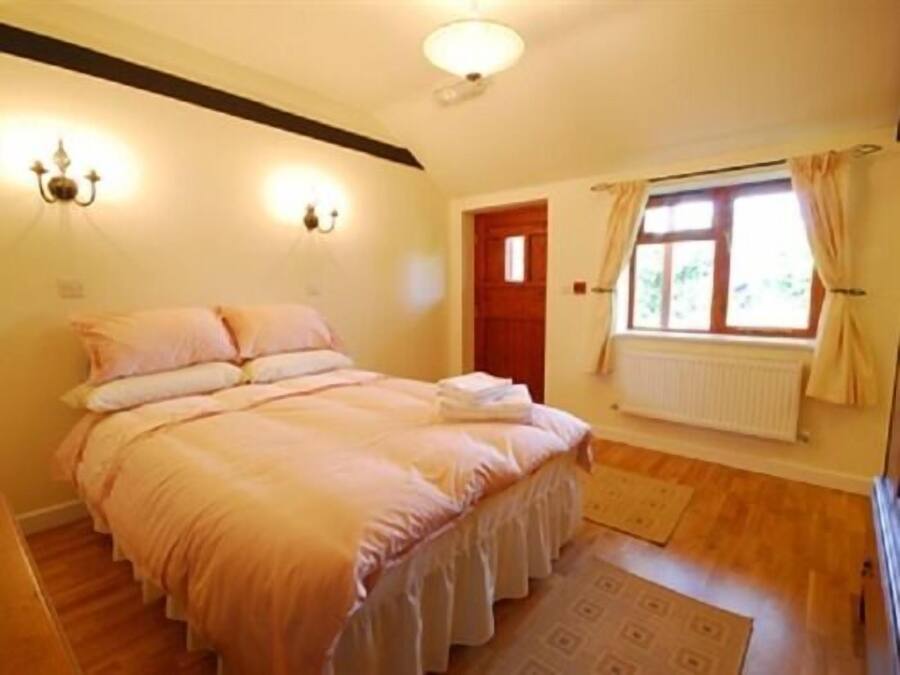 A bedroom with a bed, a window with curtains, a radiator, and a wall-mounted light fixture.