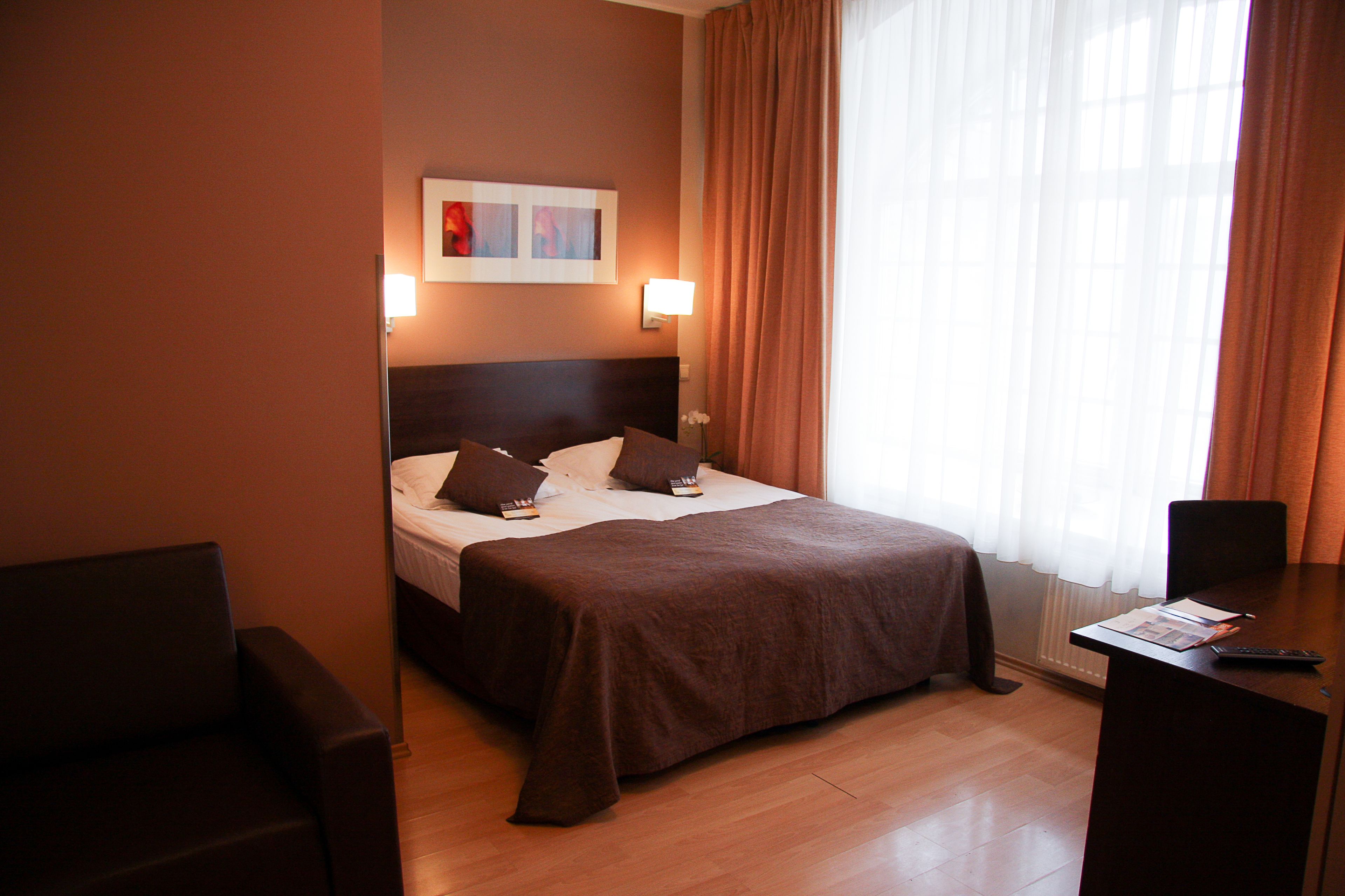 A hotel room with a bed, bedside table, and a desk with a chair.