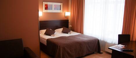 A hotel room with a bed, bedside table, and a desk with a chair.
