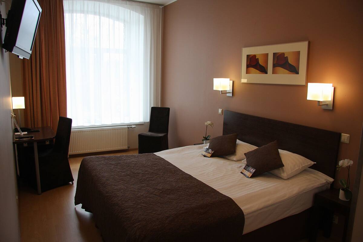 Ett hotellrum med en stor säng, ett skrivbord, en stol och en tv på väggen.