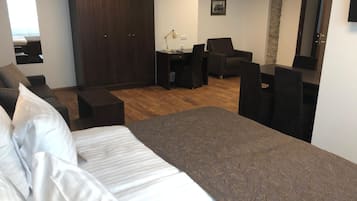 Ein Hotelzimmer mit einem großen Bett, einem Schreibtisch mit Stuhl, einem Kleiderschrank und einer Sitzecke mit Sofa und Sesseln.