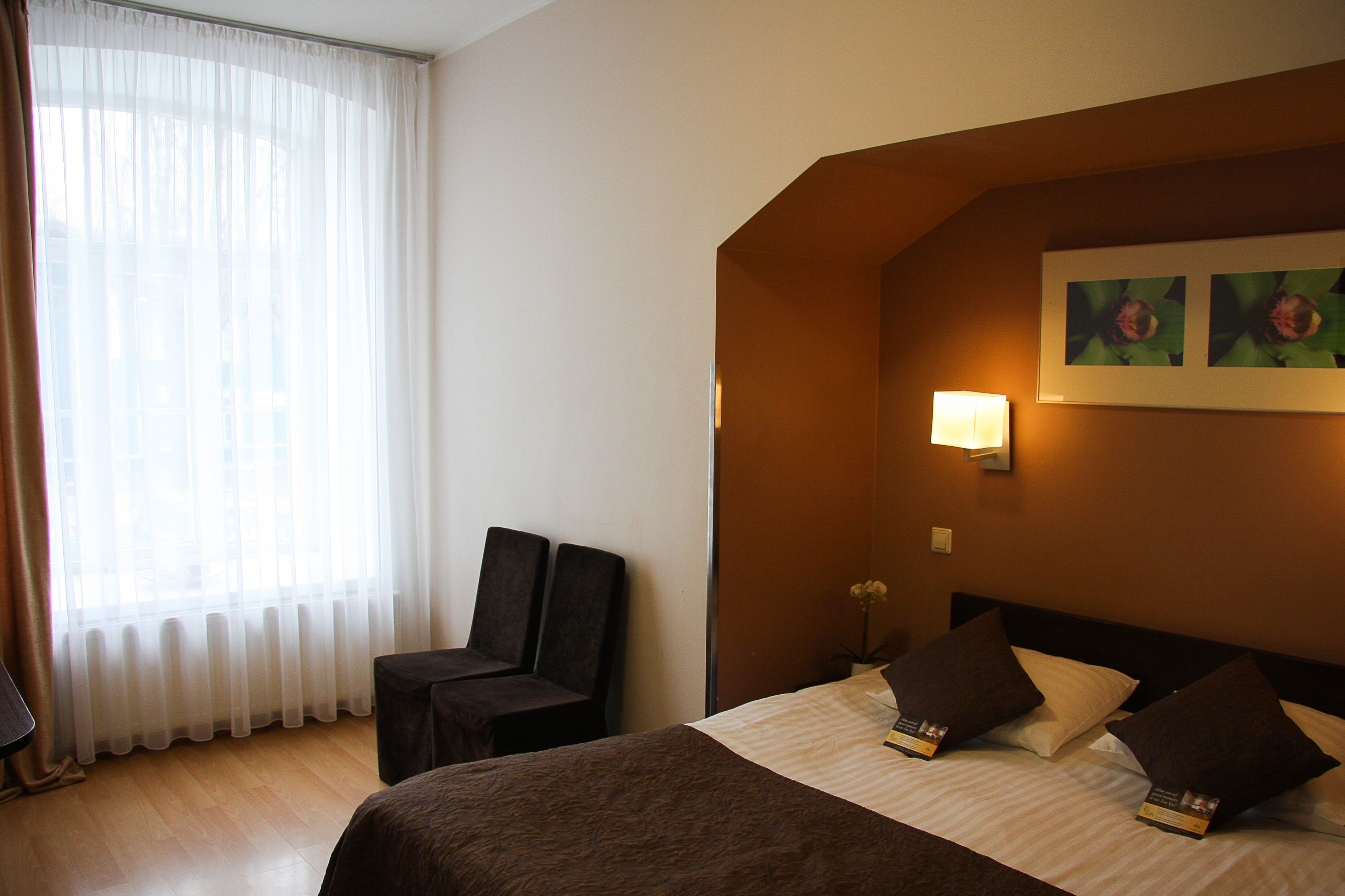 A hotel room with a bed, two chairs, a table, a lamp, and a window with curtains.