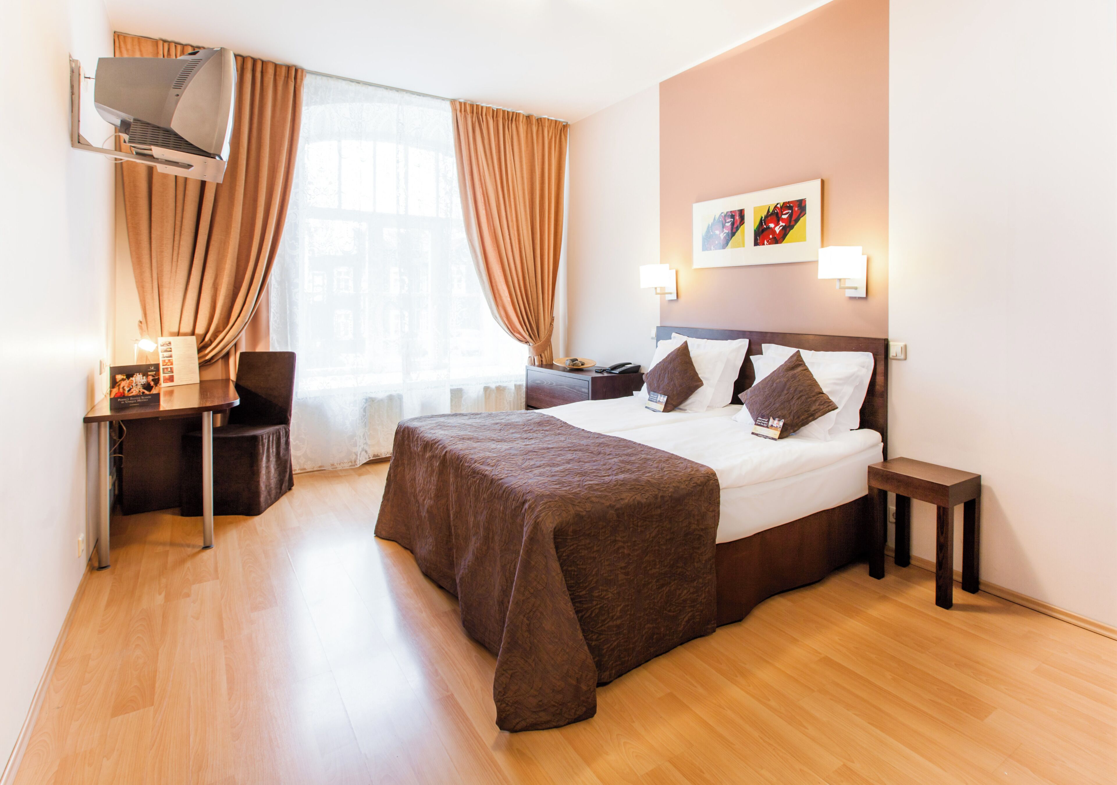 Une chambre d’hôtel comprenant un lit, des tables de chevet, un bureau, une chaise, une fenêtre avec des rideaux et un climatiseur fixé au mur.
