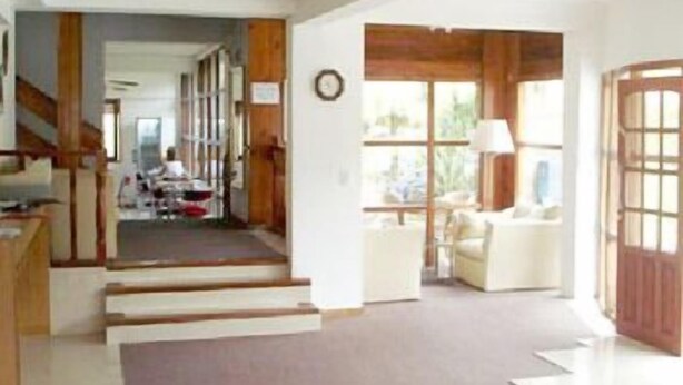 A spacious interior with a staircase leading to a dining area, a living room with a sofa and a lamp, and a wooden door. - San Remo Viking Hotel (Pinamar)