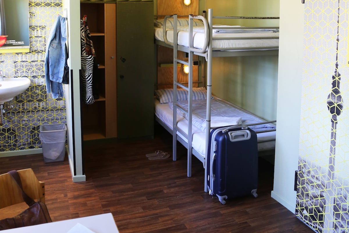 A bunk bed room with a suitcase, a sink, and a wooden floor.