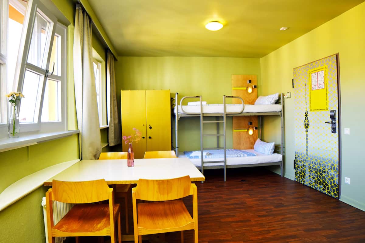A room with bunk beds, a table with chairs, a window with curtains, and a door with a pattern.