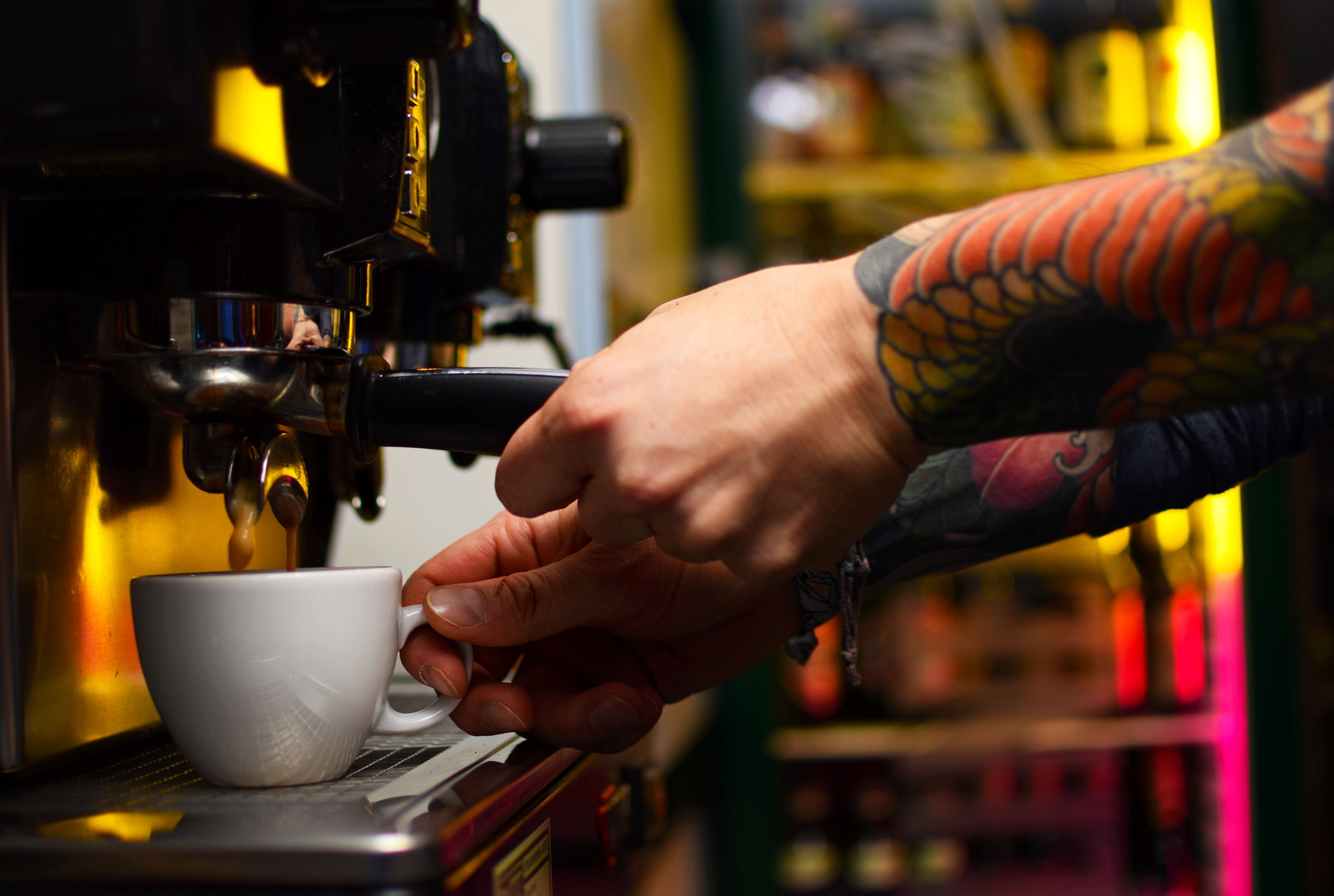 Une main tenant une tasse blanche près d’une machine à café.