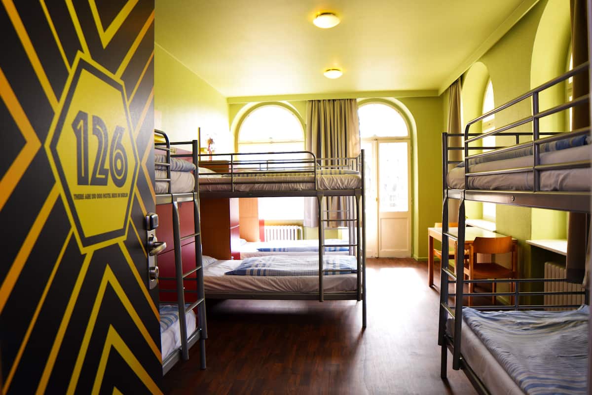 A dormitory room with bunk beds, a desk, and a chair.