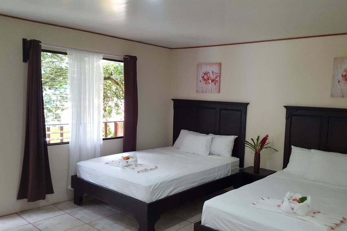 A hotel room with two beds, a window with curtains, and floral artwork on the walls.