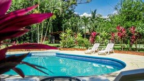 A pool area with lounge chairs and a table, surrounded by tropical plants and trees. - Lavas del Arenal (Peñas Blancas)