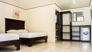 A bedroom with two beds, a tiled floor, a door leading to a bathroom, and a refrigerator with a sticker. - Lavas del Arenal (Peñas Blancas)