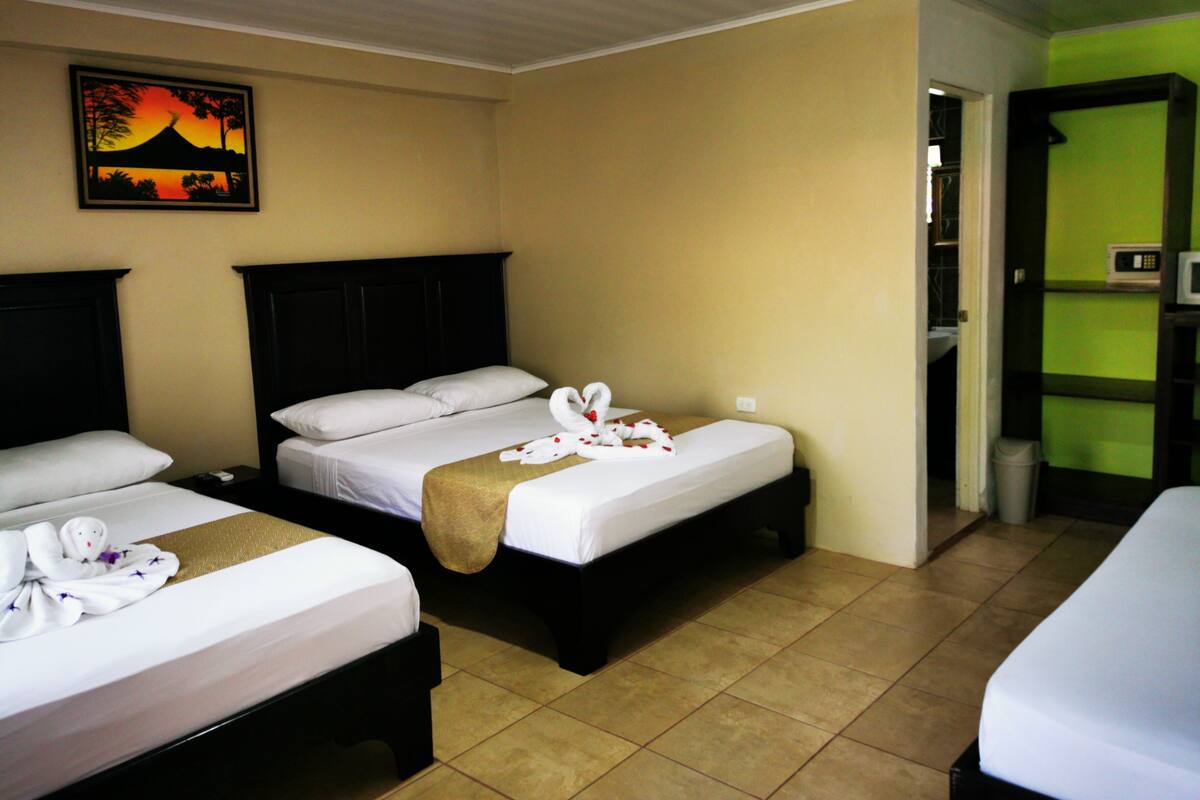 A hotel room with two beds, a headboard, a wall-mounted TV, and a green wall.