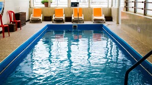 An indoor swimming pool with blue water, surrounded by orange chairs and red chairs.