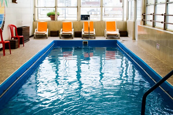 En inomhuspool med blått vatten, omgiven av orangea och röda stolar.