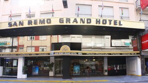 The exterior of the San Remo Grand Hotel with a signboard indicating amenities such as a conference room, spa, and restaurant.